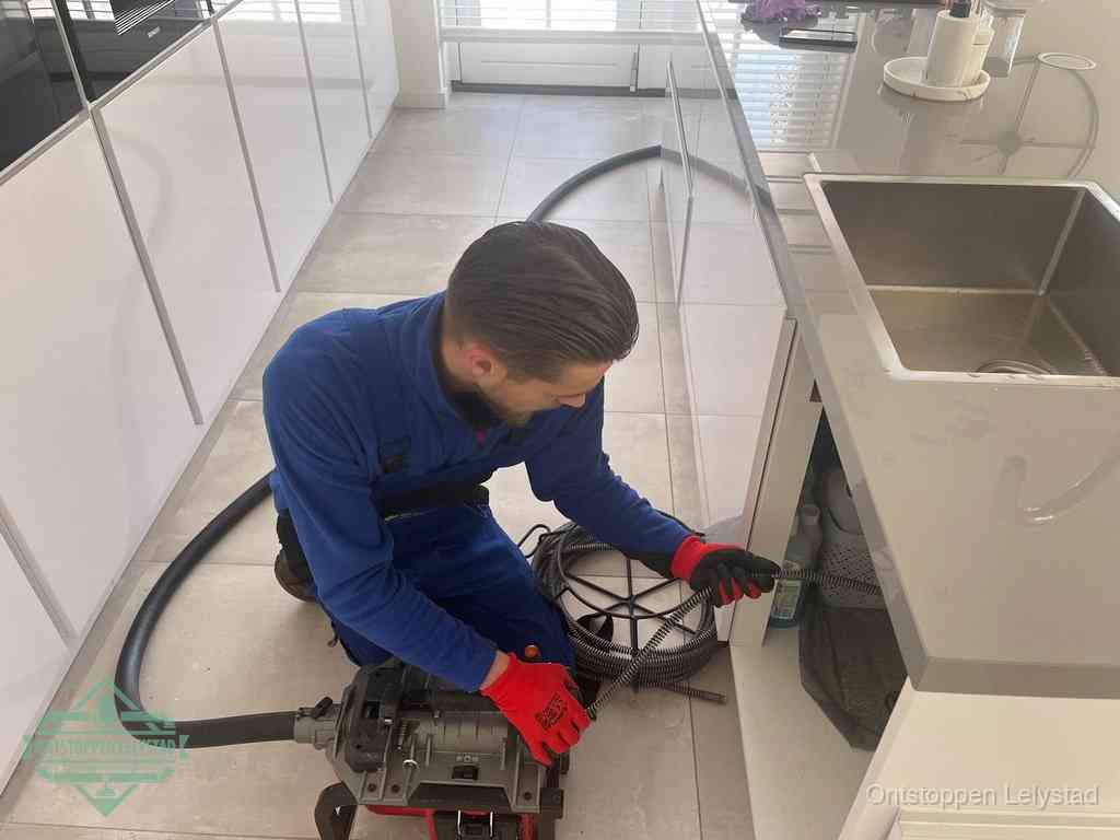 Een monteur ontstopt de keukenafvoer onder de spoelbak met een elektrische veermachine in Lelystad