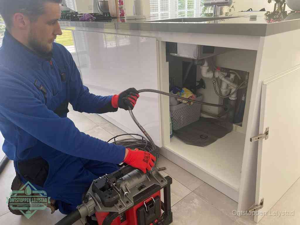 Monteur voert een ontstoppingsveer in de afvoer onder de keuken in Lelystad