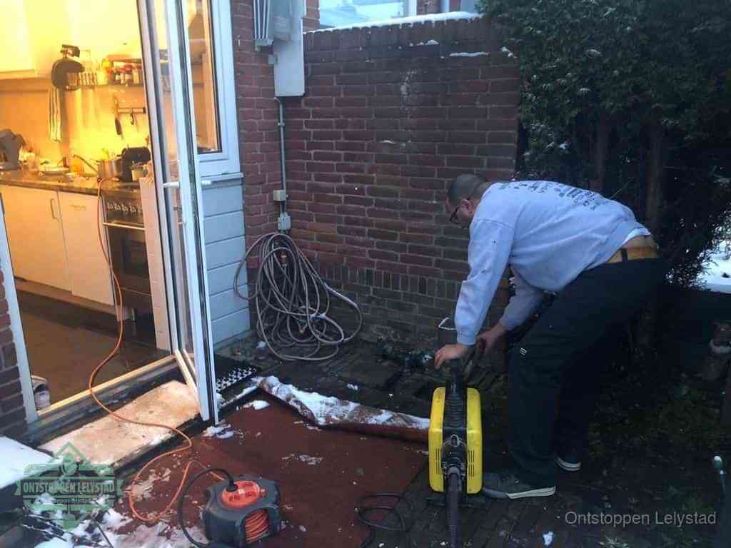 Een monteur werkt buiten bij een open riool-/grondput met een elektrische ontstoppingsmachine om een verborgen afvoerprobleem op te sporen in Lelystad