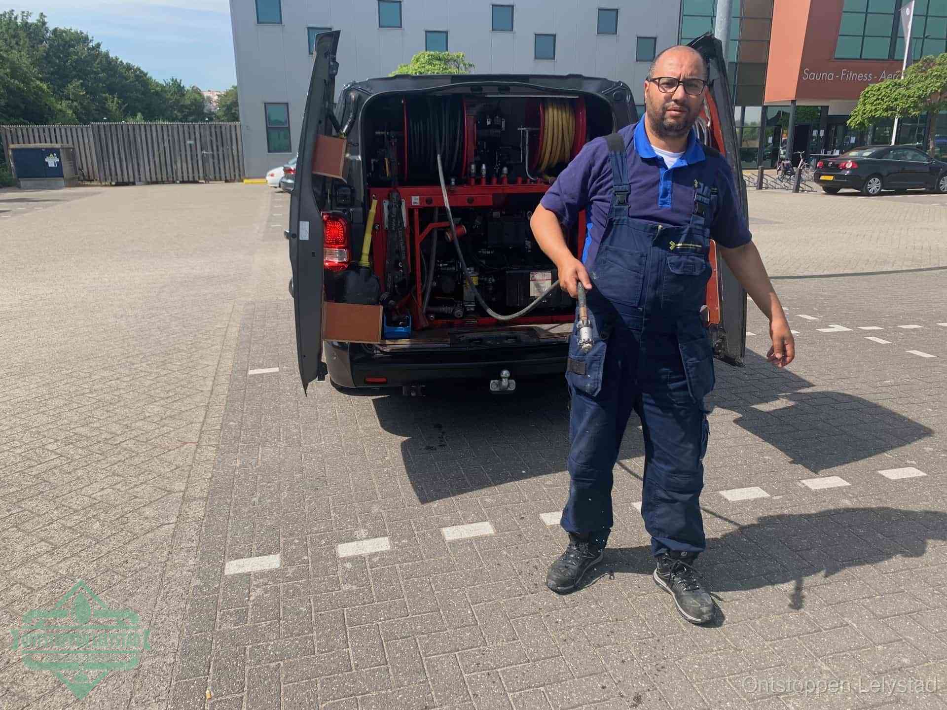 Een monteur bij zijn bestelbus met een hogedruk- en rioolreinigingsunit, klaar om de oorzaak van terugkerende wc-verstoppingen aan te pakken in Lelystad