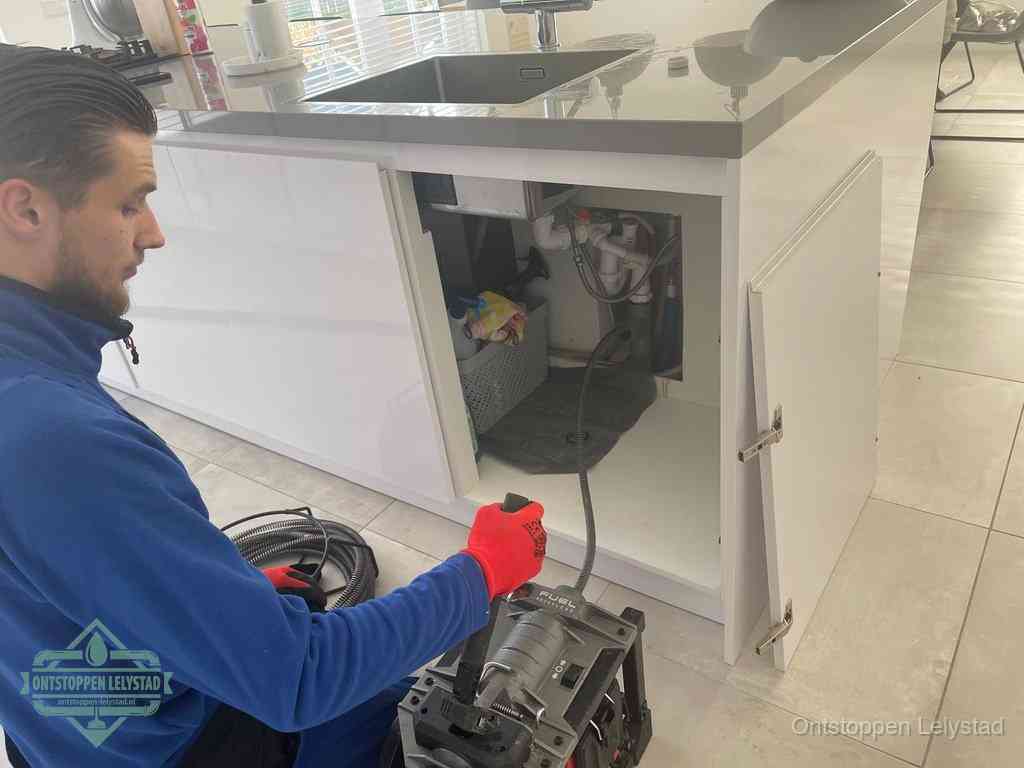 Monteur ontstopt met een veermachine een verstopte afvoer onder de gootsteen in Lelystad