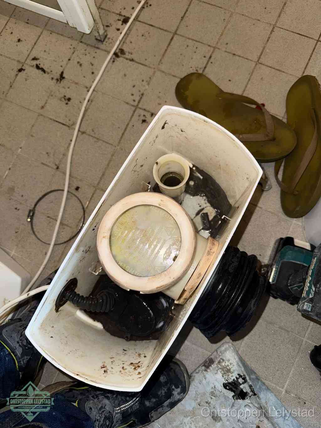 Een gedemonteerde toiletpot op de vloer met ontstoppingsveer en gereedschap ernaast, het verwijderen van een vastzittend voorwerp uit de wc in Lelystad