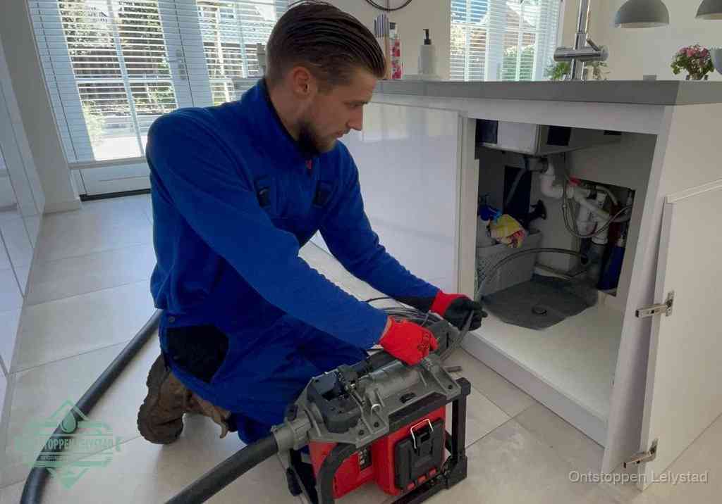 Een monteur voert een professionele elektrische ontstoppingsmachine in de afvoer onder de spoelbak tijdens het gootsteen ontstoppen in Lelystad